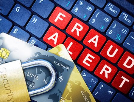 El teclado de una computadora muestra la frase "Alerta de fraude" en rojo, blanco y azul, con dos tarjetas de crédito y un candado de seguridad en la parte superior para implicar conocimiento de los estafadores.