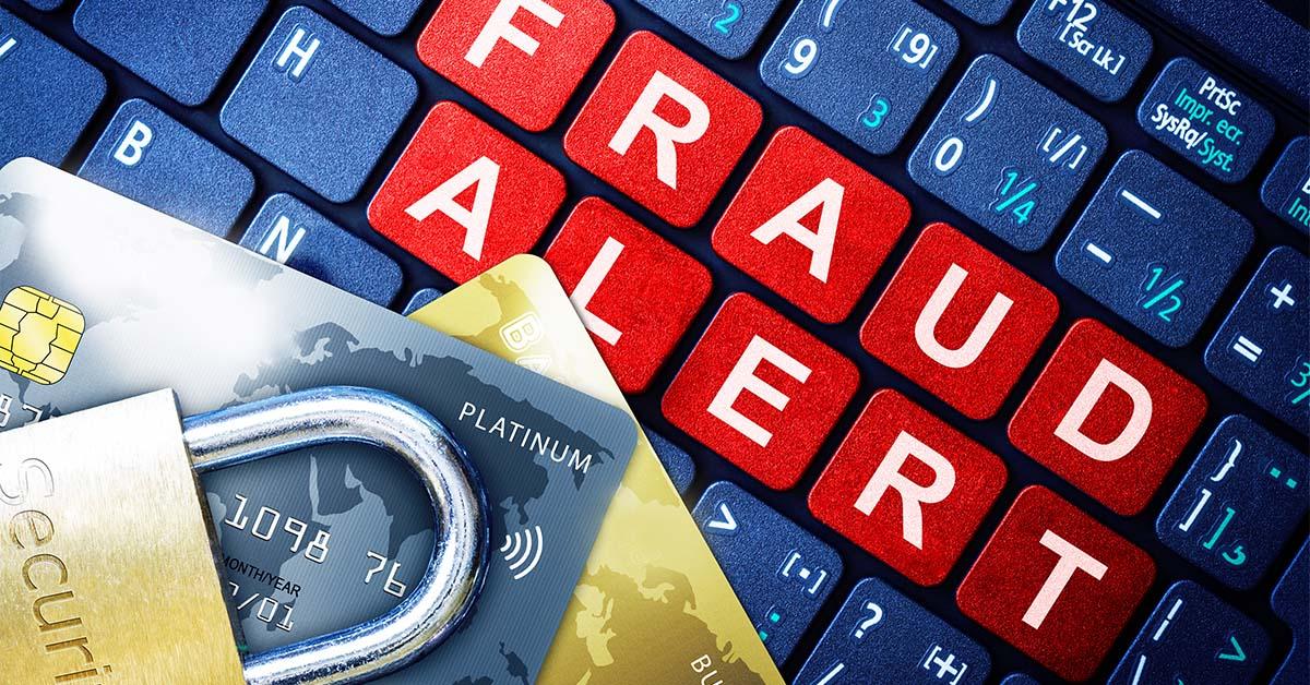 電腦鍵盤上以紅、白、藍三色顯示出「詐騙警報」字樣，上面放置了兩張信用卡和一把安全鎖，以提醒人們警惕詐騙。